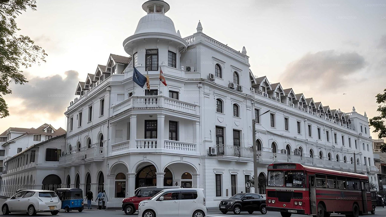 White colonial-style building with a red bus in front, under a cloudy sky.