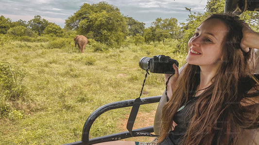 A person smiling while on a safari in Udawalawe National Park, with a elephant in the background.